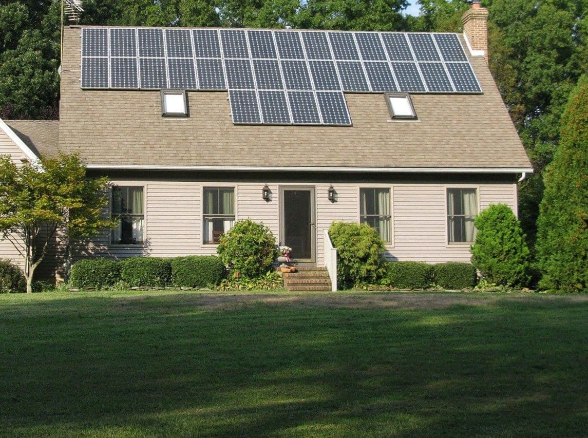 A tan house with solar panels on the roof and single-hung windows.