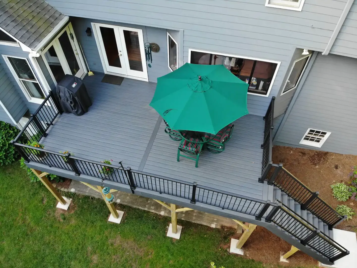 An overhead view of a gray deck with black railings and patio furniture with a green umbrella.