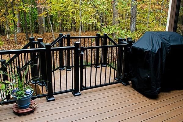 A brown deck with black railings overlooking a wooded yard.