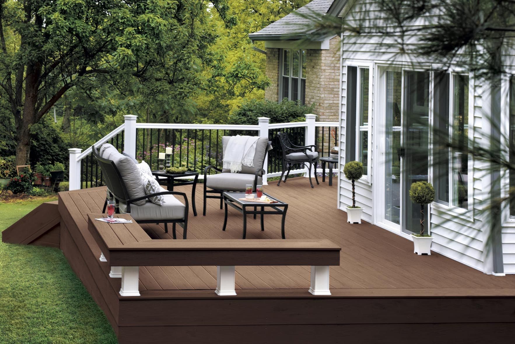 A brown TimberTech deck with a black and white railing, built-in bench, and patio furniture.