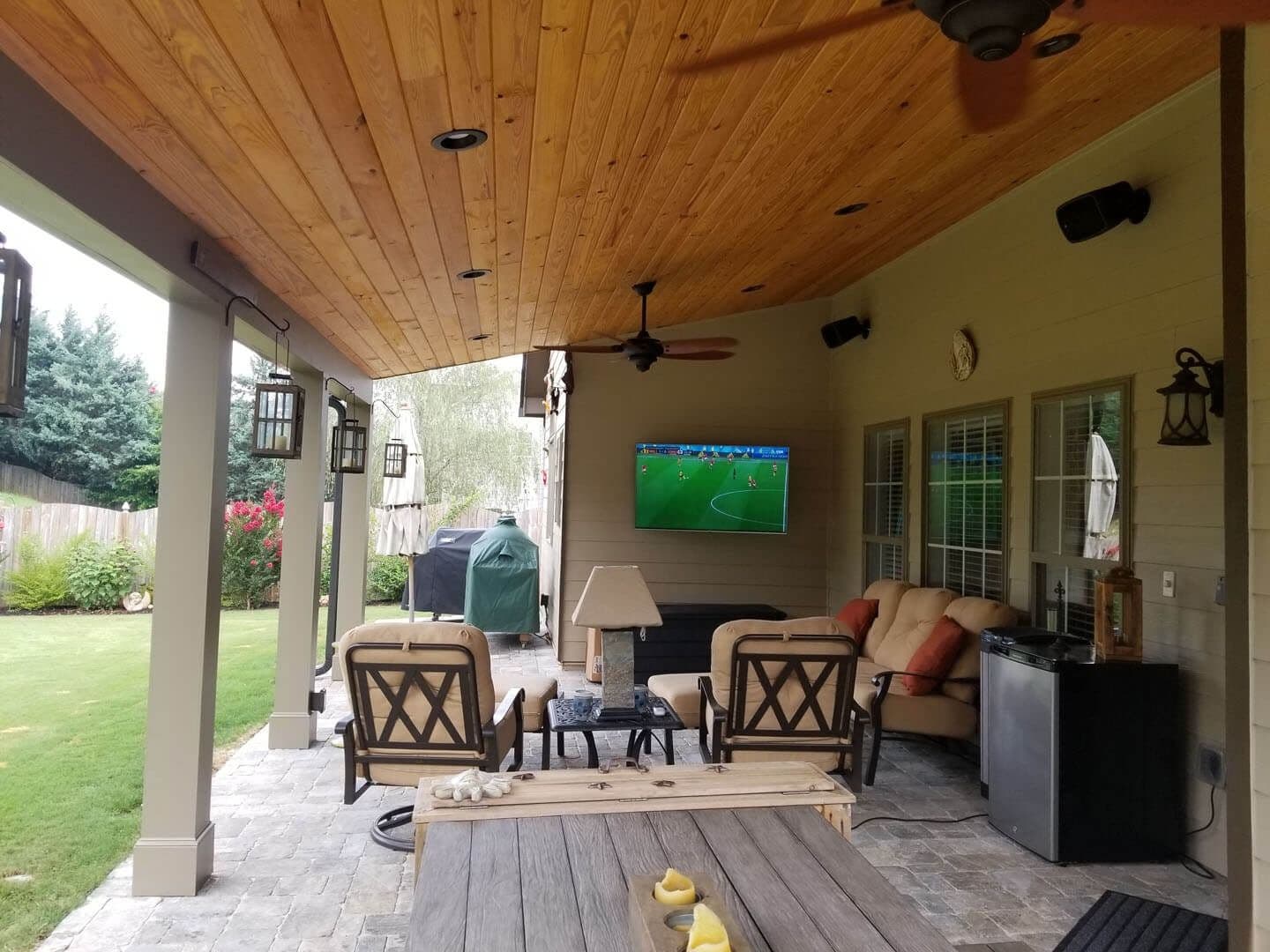 A covered porch with patio furniture, a TV, and black ceiling fan by Outback Deck.