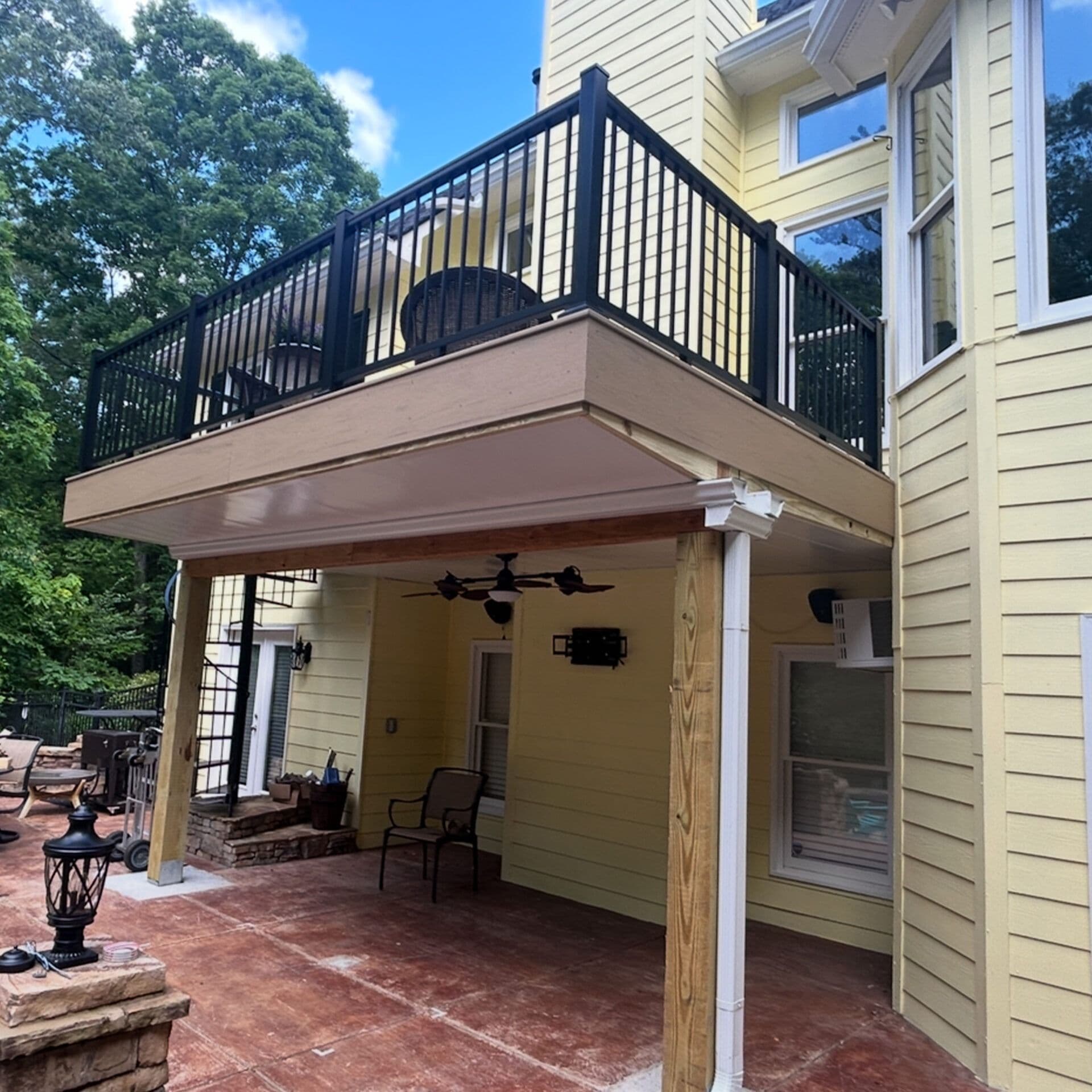 A second-story brown deck with black railing by Outback Deck.