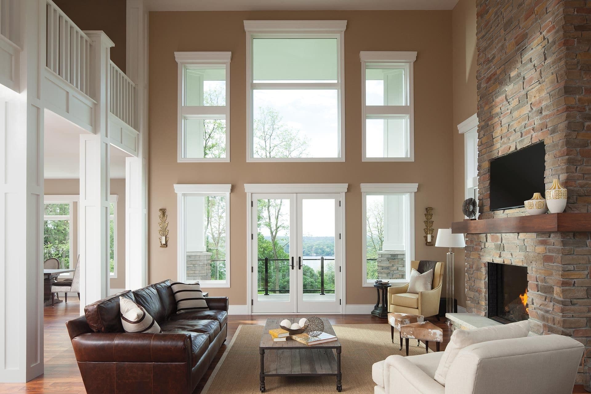 A tan living room with high ceilings, multiple large picture windows, and white double patio doors.