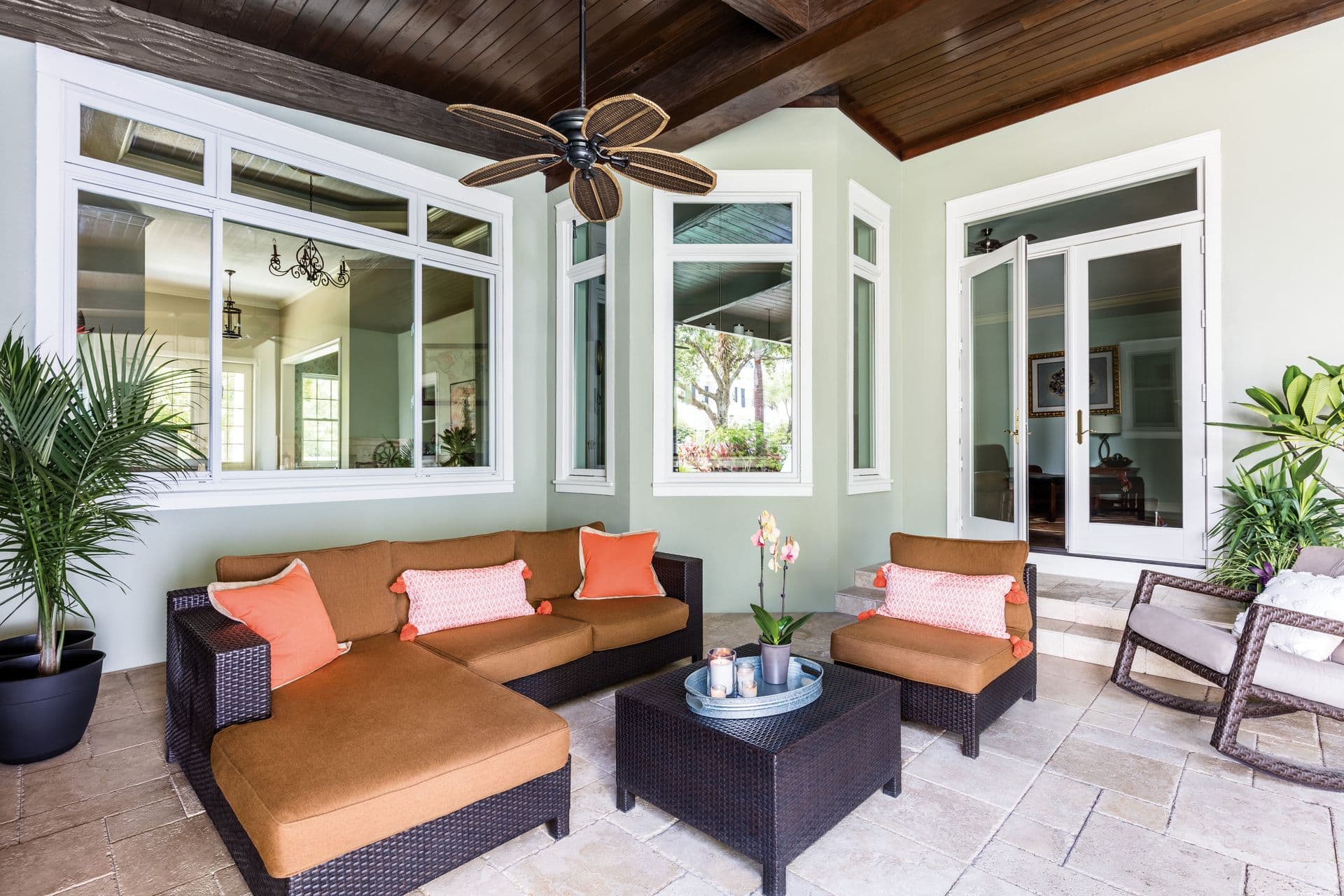 A covered porch on a light gray house with multiple picture and casement windows, a bay window, and double patio doors.