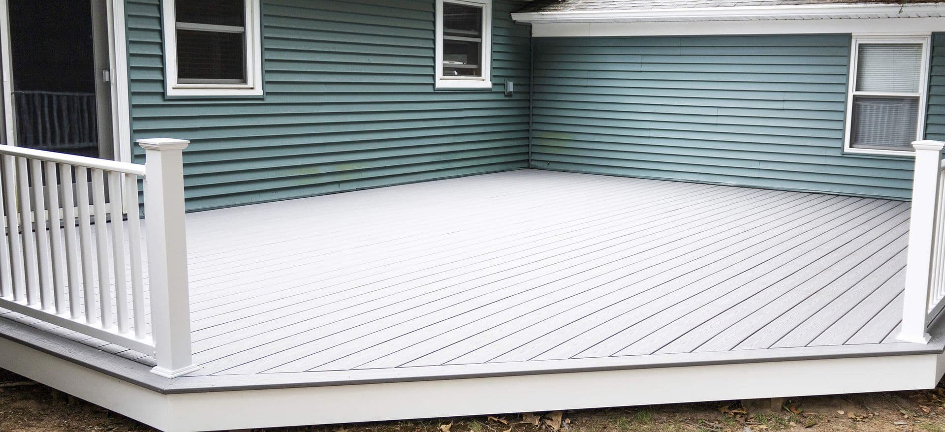 A light gray composite deck with white railings off a blue house.