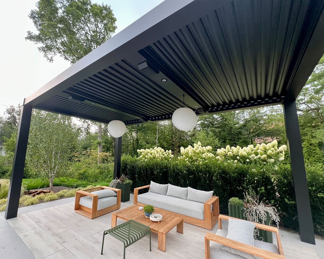 A black, louvered StruXure pergola with built-in lighting over a stone patio with gray patio furniture.
