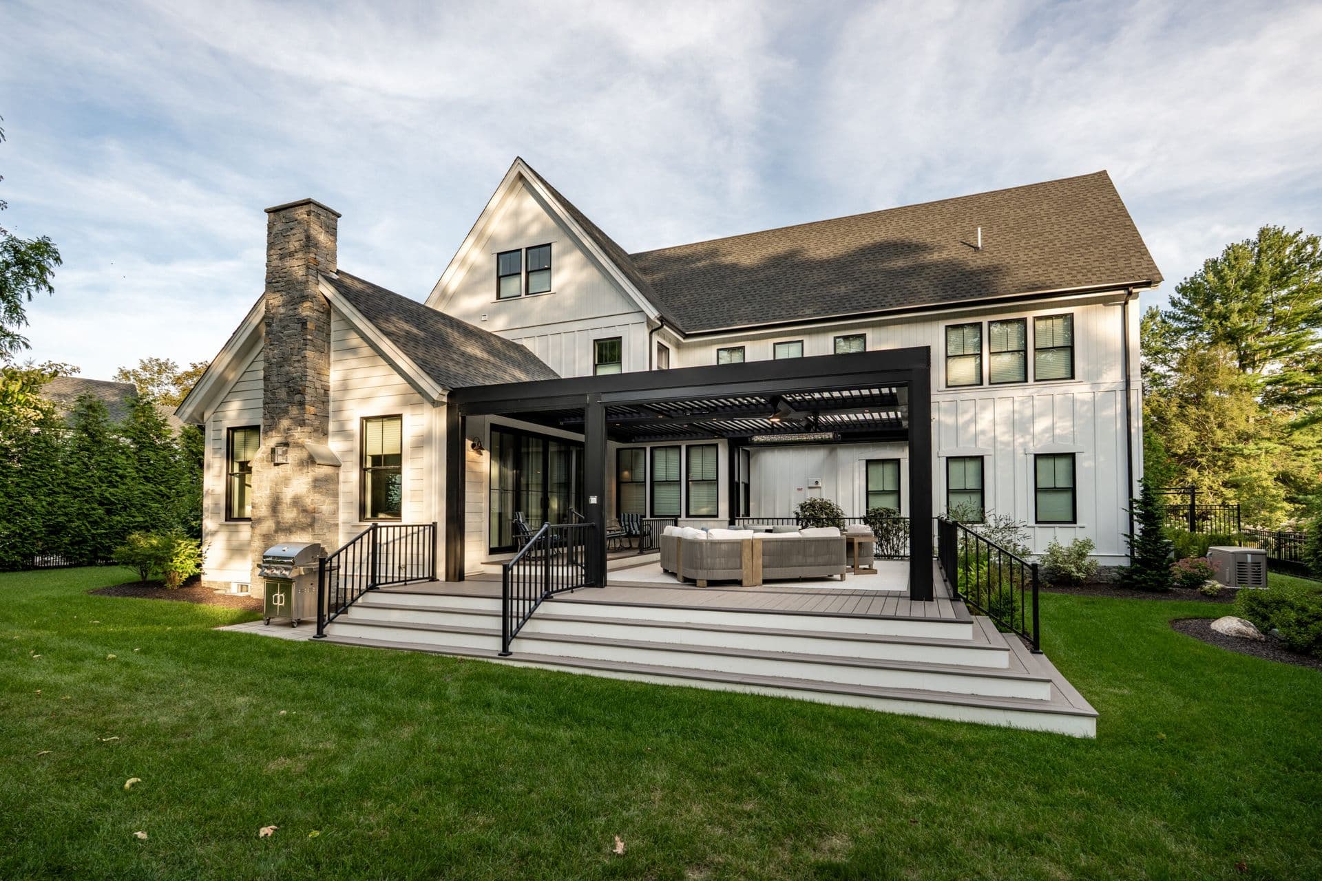 A black motorized louvered pergola over a back deck with patio furniture off of a white house.