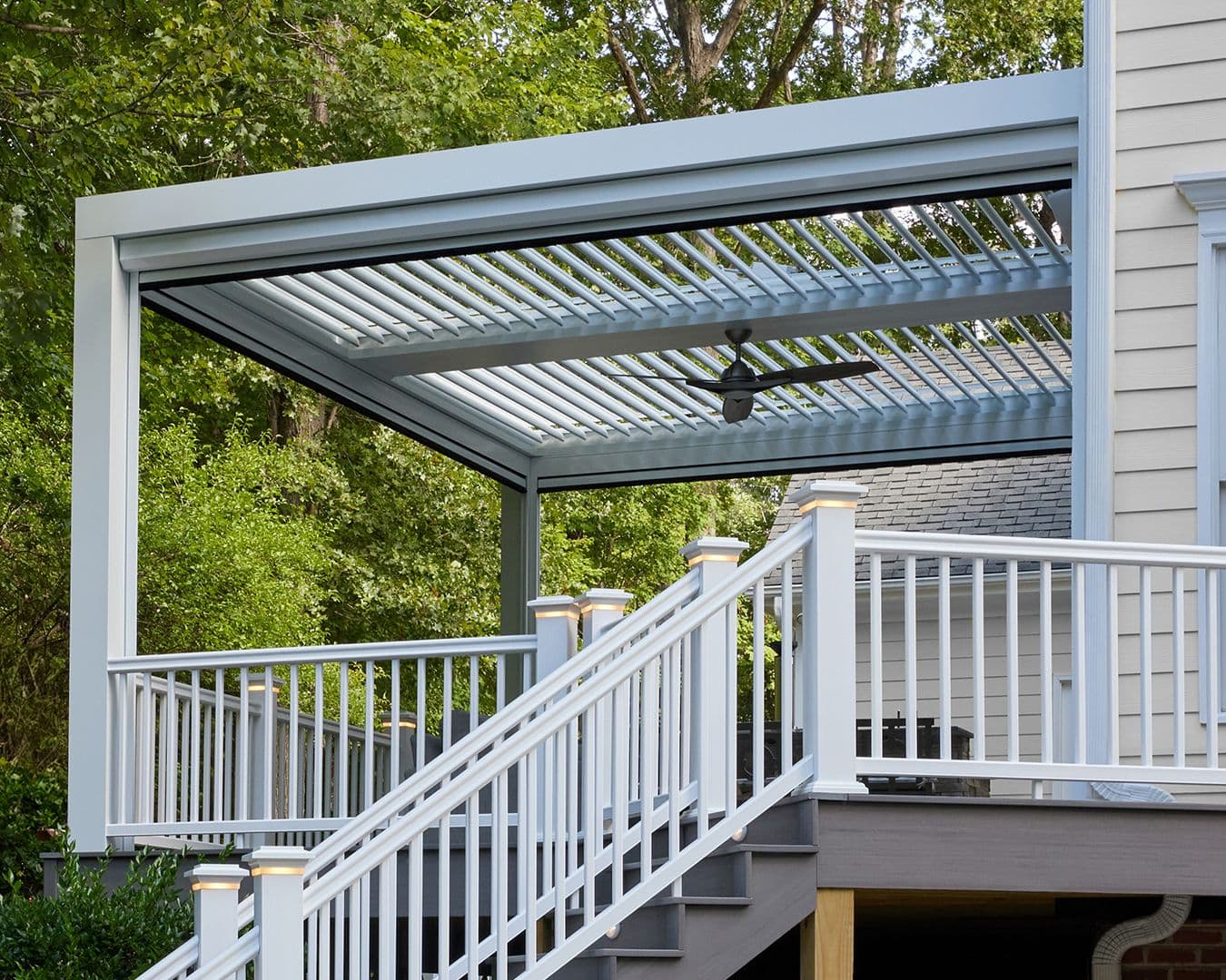 A white StruXure louvered pergola with a ceiling fan over a gray deck.
