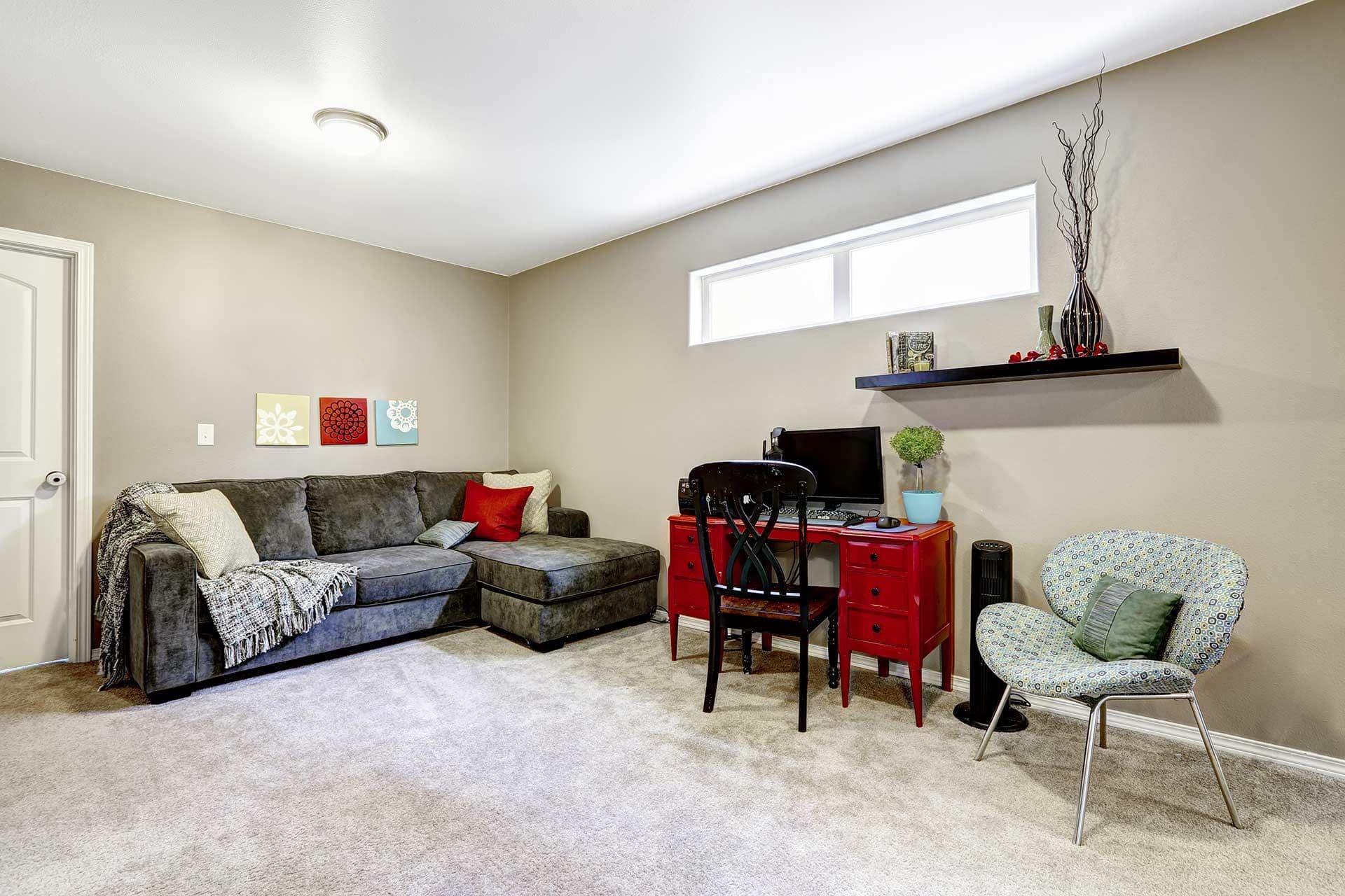 A finished basement with gray couch and hopper windows.