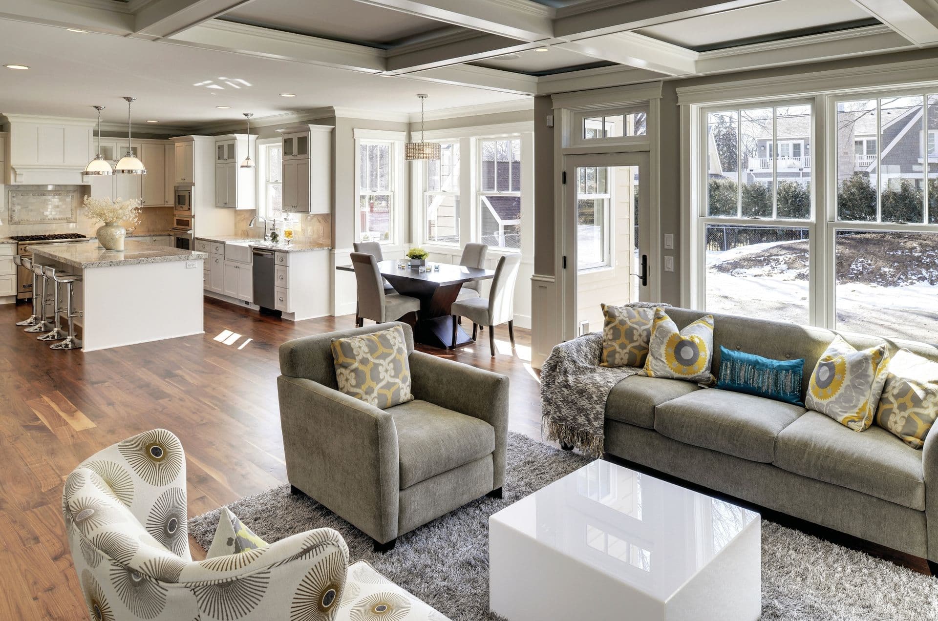 A gray living room with double-hung windows and a kitchen in the background.
