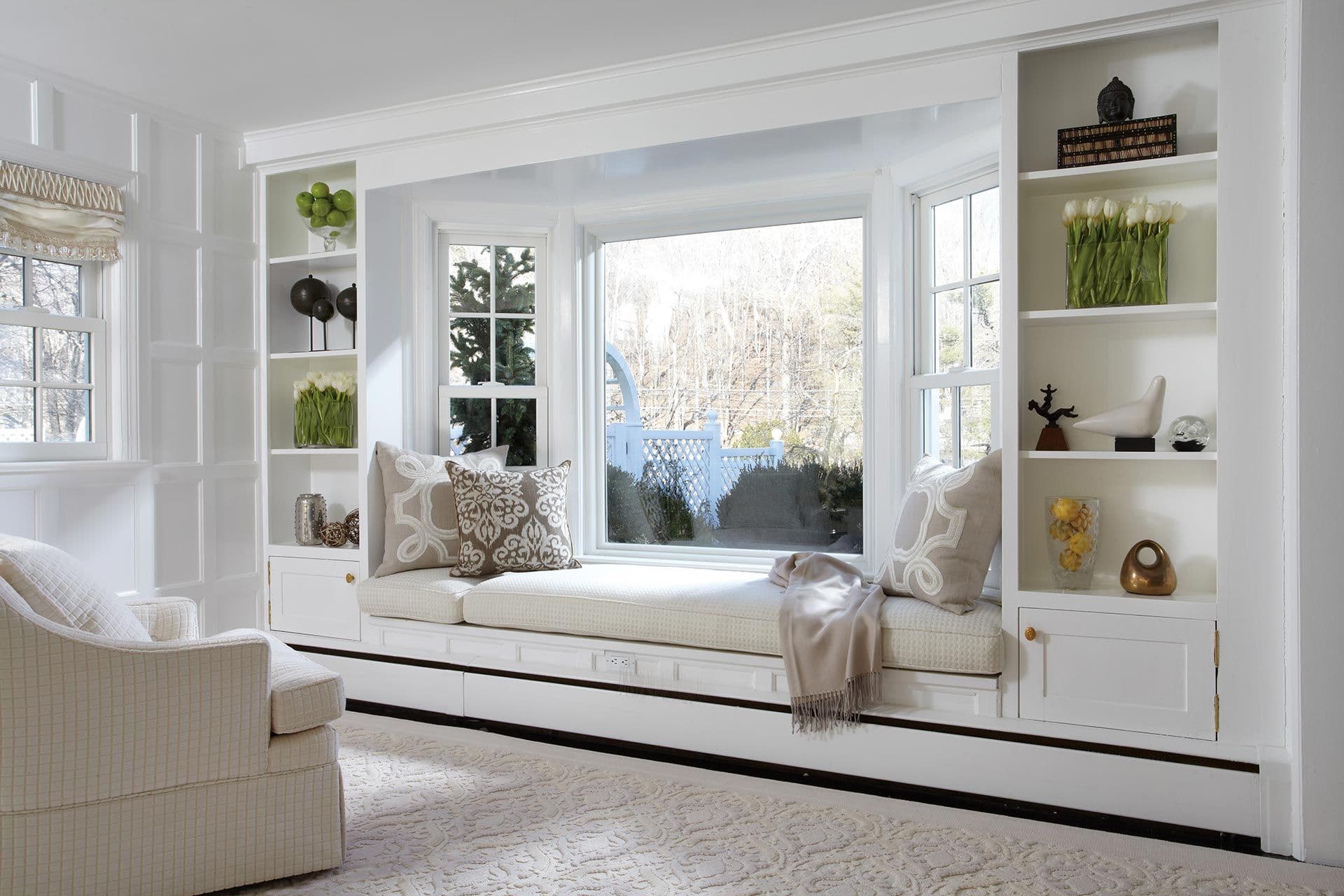 A white living room with built-in shelving and a bay window with single-hung lites.