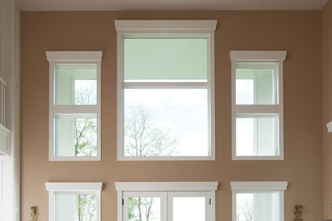 A tan living room with high ceilings and multiple large picture windows.